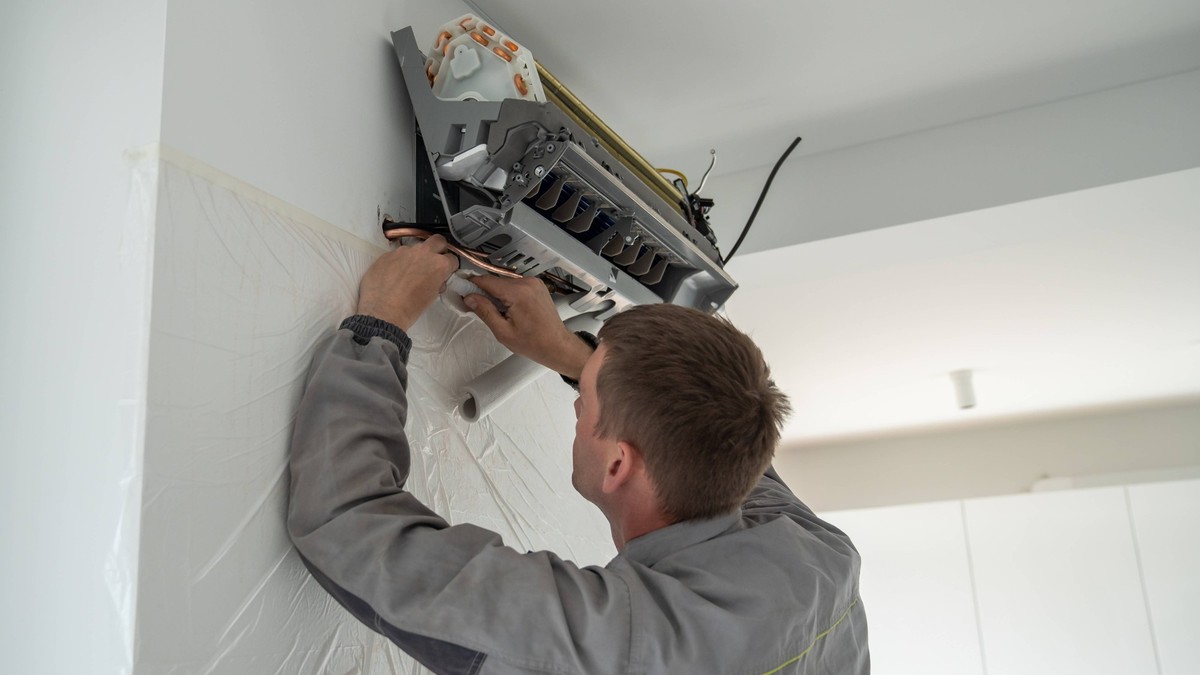 Professioneller Techniker in Uniform bei der Installation einer Klimaanlage in einer modernen Wohnung. Professioneller Techniker in Uniform bei der Installation einer Klimaanlage in einer modernen Woh ...