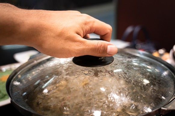 Action of people hand is preparing to open the Sukiyaki/Shabu Shabu pottery&#039;s lid after water already boiled. Selective focus photo.