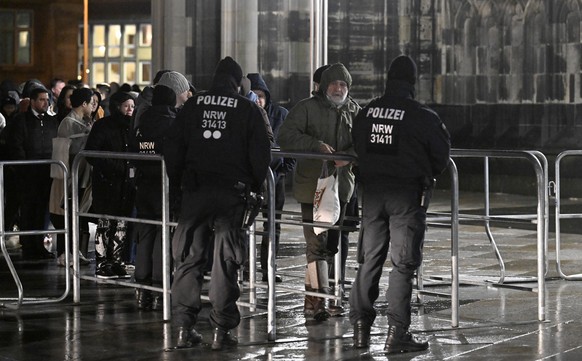 24.12.2023, Nordrhein-Westfalen, Köln: Polizisten sichern einen Eingang am Kölner Dom. Aufgrund von Hinweisen auf einen geplanten islamistischen Anschlag hat die Polizei die Sicherheitsmassnahmen hoch ...