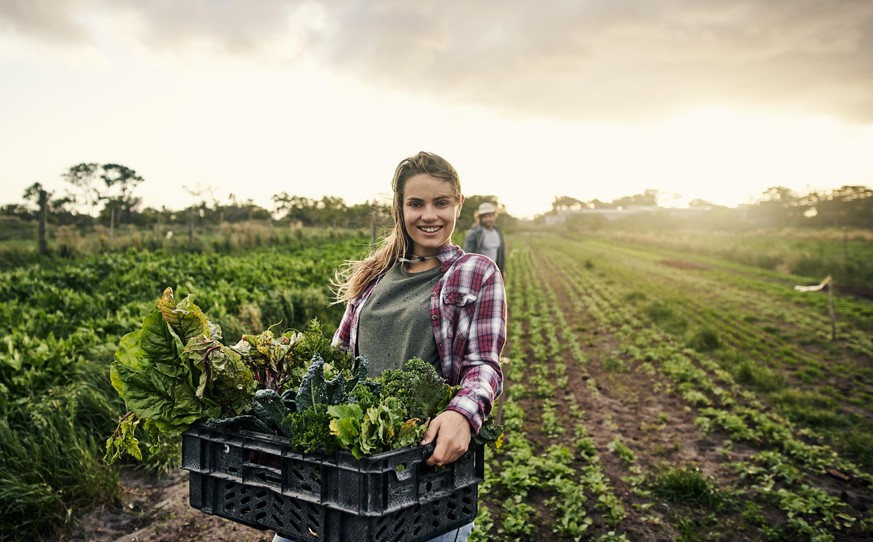 Shot of a young woman holding a crate of freshly picked produce on a farm