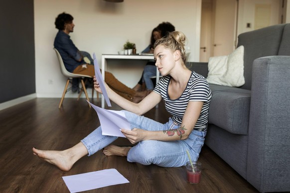 Young woman sitting on floor with papers and friends in background model released Symbolfoto property released PUBLICATIONxINxGERxSUIxAUTxHUNxONLY VABF01783