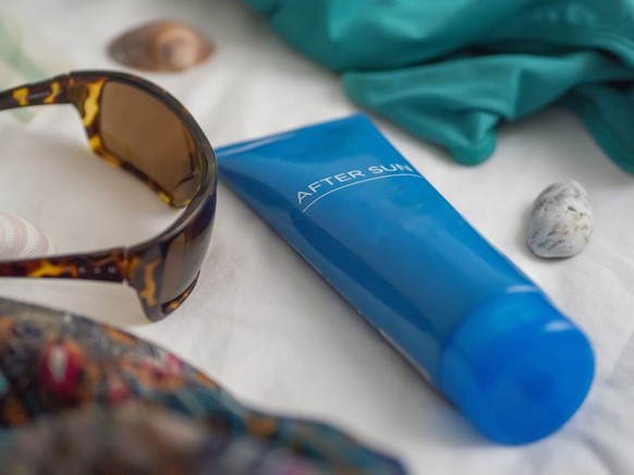 A bottle of blue after-sun lotion for summer sunburns, a skincare routine after a beach vacation. Closeup of a body cream treatment for tanning and moisturizing. Sea essential flat lay with sunglasses