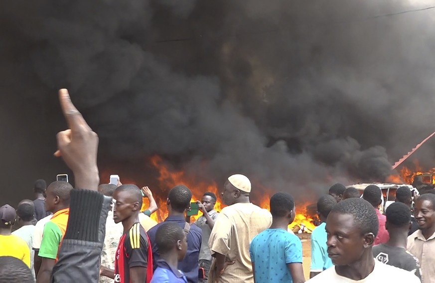 dpatopbilder - 27.07.2023, Niger, Niamey: Mit dem brennenden Hauptquartier der Regierungspartei im Rücken demonstrieren Anhänger meuternder Soldaten. Das Militär im Niger hat erklärt, die Forderung de ...
