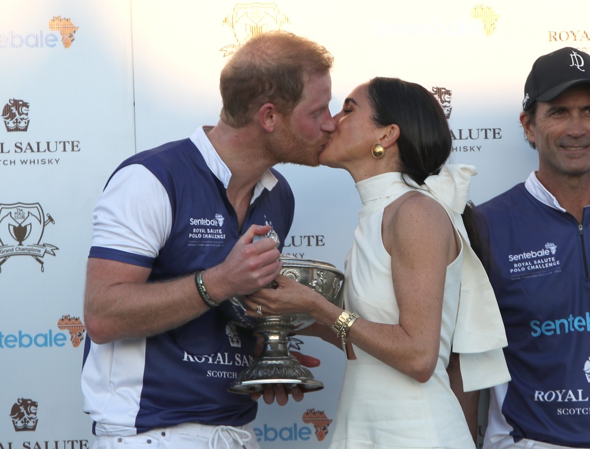 12.04.2024, USA, Wellington: Der britische Prinz Harry (l), und seine Frau Meghan, Herzogin von Sussex, k�ssen sich, w�hrend sie seinem Polo-Team die Troph�e f�r den Sieg bei der Royal Salute Polo Cha ...