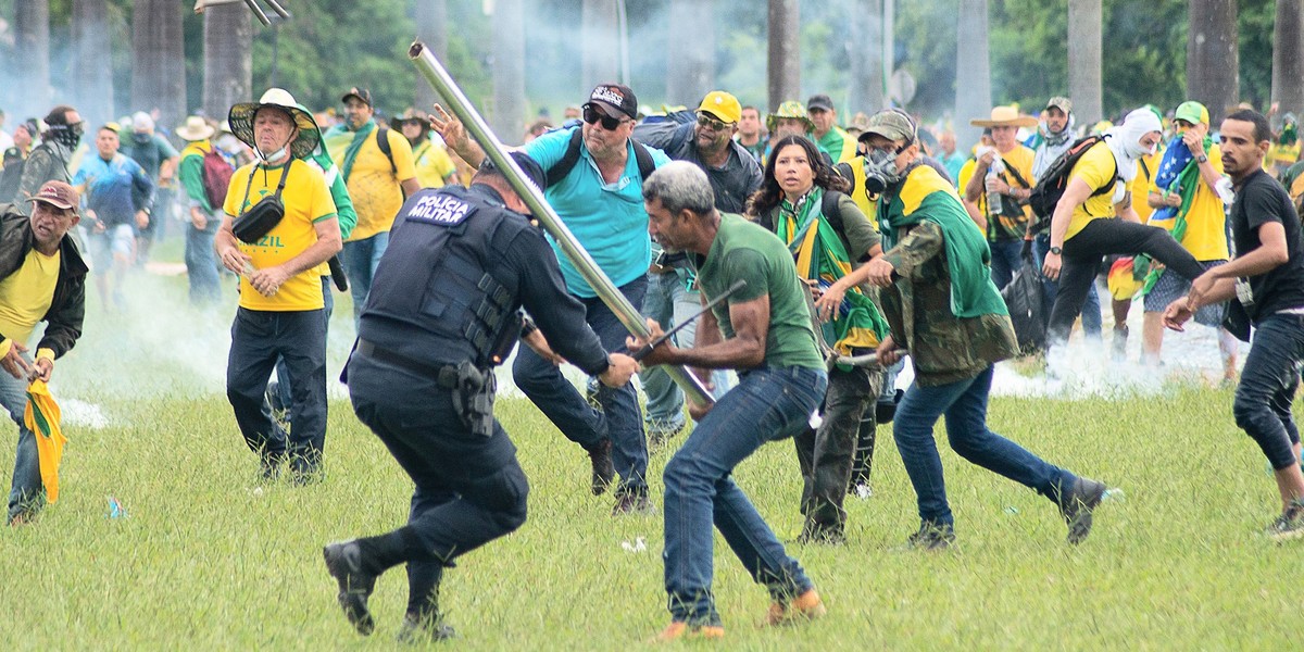 08.01.2023, Brasilien, Brasilia: Anh�nger des ehemaligen brasilianischen Pr�sidenten Bolsonaro geraten in der Hauptstadt mit Polizisten aneinander. Ein Mann schl�gt dabei einen Polizisten mit einer St ...