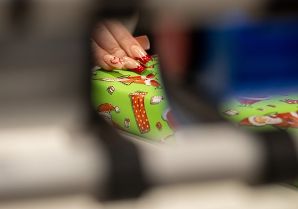 ARCHIV - 09.12.2023, Baden-Württemberg, Ulm: In einem Kaufhaus verpackt eine Verkäuferin für Kunden ein Weihnachtsgeschenk. (zu dpa &quot;Handelsverband zieht durchwachsene Bilanz des Weihnachtsgeschä ...