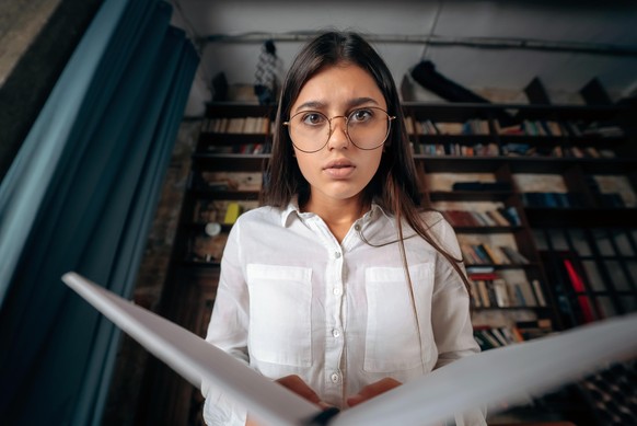 Young woman holding an open book in hands and looking at the camera || Modellfreigabe vorhanden