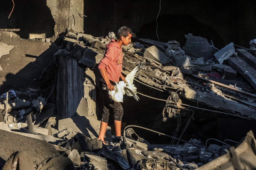 15.12.2023, Palästinensische Gebiete, Rafah: Ein Junge hält Tauben in der Hand, während er nach einem israelischen Luftangriff auf ein Haus der Familie Al-Arja in der Stadt Rafah im südlichen Gazastre ...