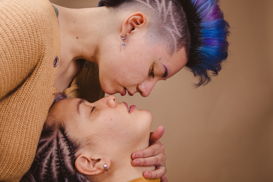 Lgbt and gay concept. Close up of a lesbian couple kissing. Detail of the lips of two women about to kiss in pastel peach background