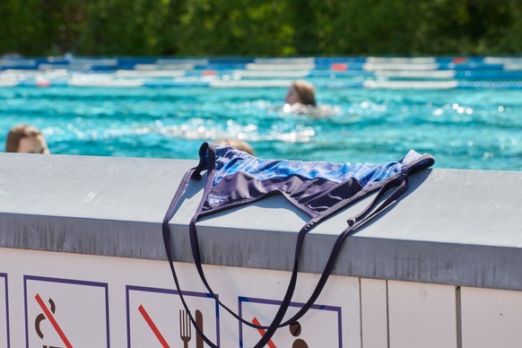 ARCHIV - 11.04.2019, Berlin: Ein Badeanzug liegt auf einer Mauer im Prinzenbad, dahinter schwimmen Menschen im Becken ihre Bahnen. Oben rum frei d�rfen sich im Schwimmbad bisher meist nur M�nner zeige ...