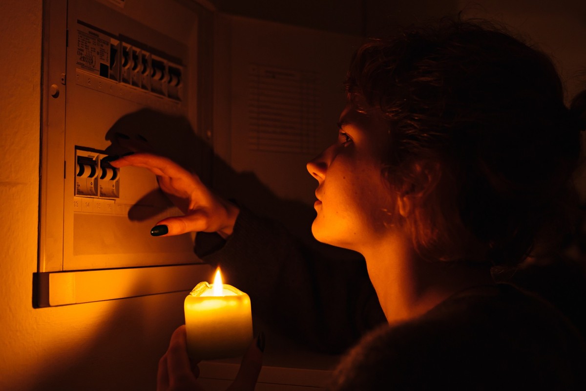 young woman with candles in complete darkness examines fuse box or electrical distribution board at home during power outage. Blackout, no electricity