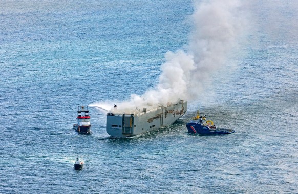 26.07.2023, Niederlande, Ameland: Eine Luftaufnahme zeigt den deutschen Notschlepper &quot;Nordic&quot; (l), der das Feuer auf einem brennenden Frachter in der Nordsee bekämpft. Rechts ist das Boot &q ...