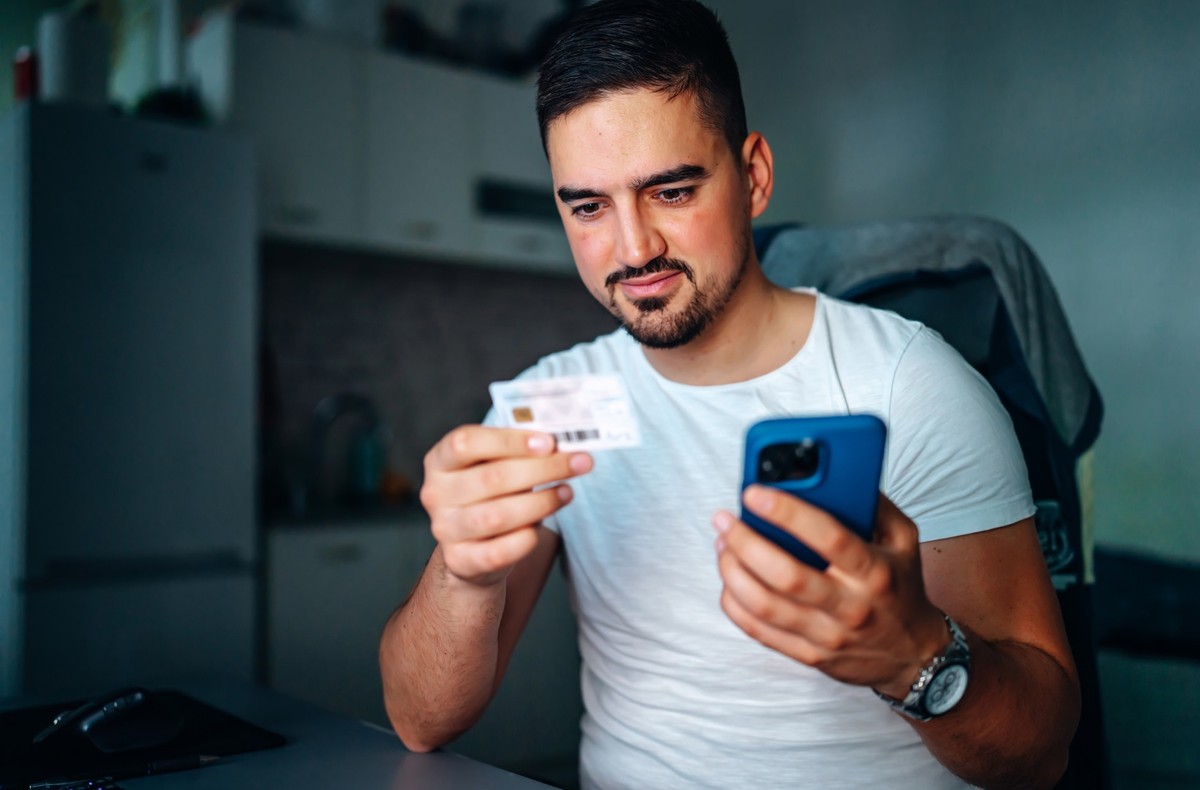 From the comfort of his home, a young man diligently transfers details from his Medicare insurance card to his mobile phone, ensuring easy access to his healthcare benefits and information, streamlini ...