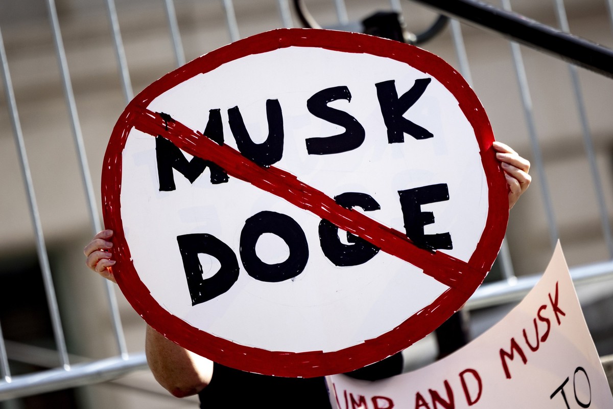 17.02.2025, USA, Los Angeles: Ein Demonstrant hält ein Plakat mit einem Verkehrsverbotsschild mit der Aufschrift &quot;Musk DOGE&quot; während einer Kundgebung gegen die Politik von US-Präsident Trump ...