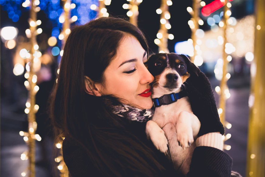 Beautiful young brunette woman with Jack Russell terrier enjoying Christmas or New Year night ona a city street.