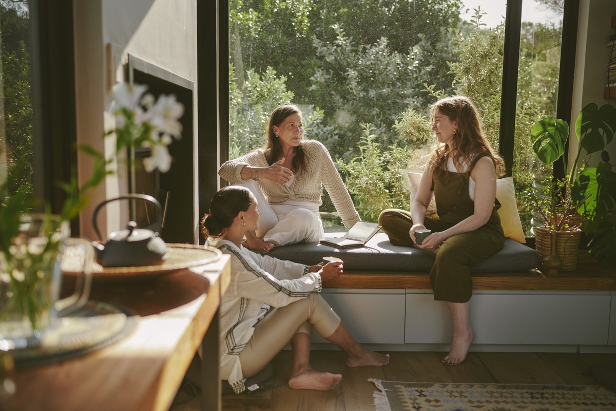 Smiling group of diverse female friends talking while sitting together at a bench by a window during a women&#039;s wellness retreat