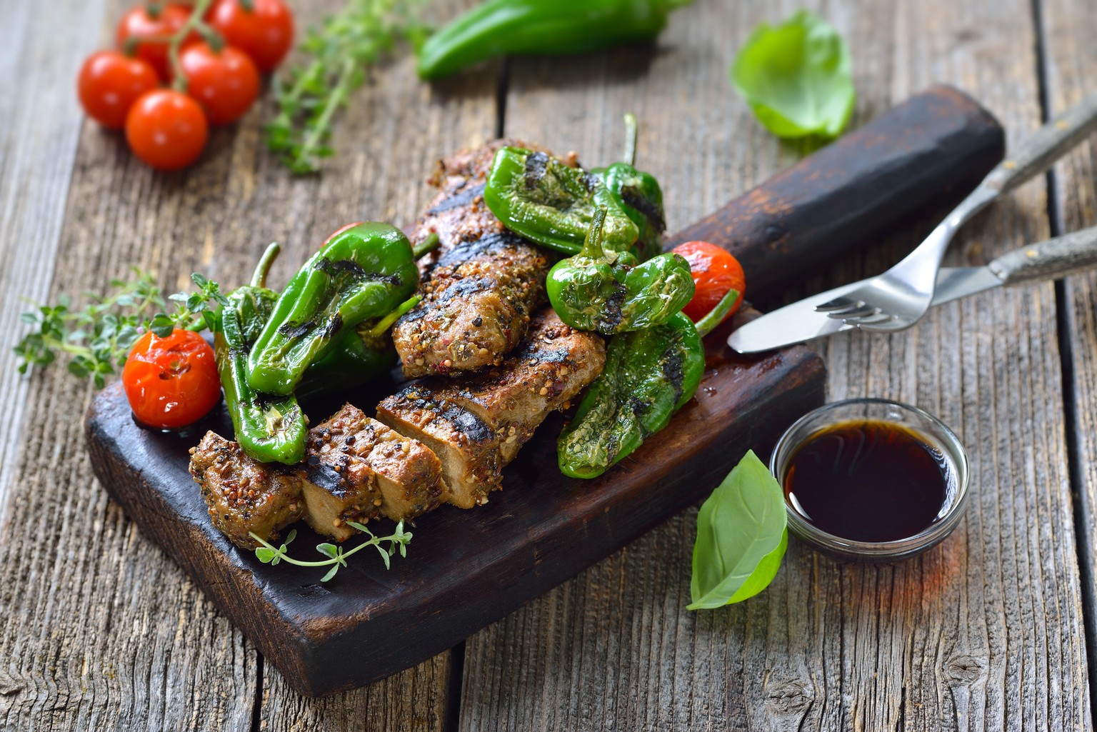 Grilled vegan seitan steaks with pimientos de padron and served with a herb soy sauce on a rustic wooden background