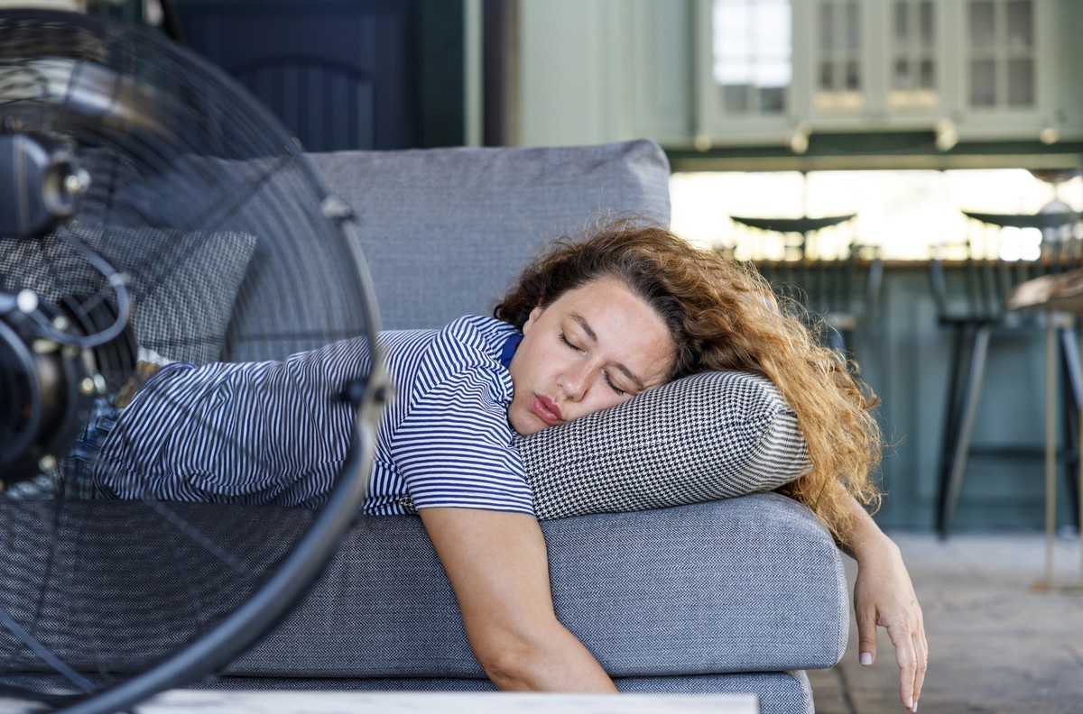 Young woman lying in front of the electric fan at home, overwhelmed by the heat