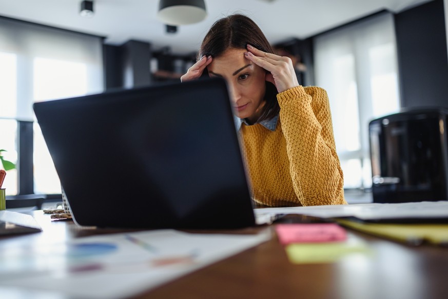 Young worried entrepreneur woman looking at laptop computer at home. Freelance woman programmer working from home