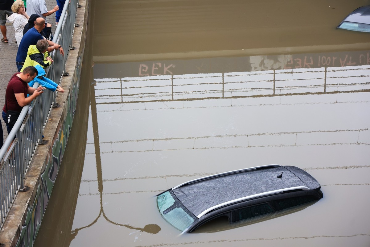 20.08.2024, Polen, Warschau: Menschen stehen auf einer Br�cke und schauen auf verlassene Autos im Hochwasser eines �berfluteten Tunnels. Die Warschauer Feuerwehr verzeichnete rund 800 Notrufe im Zusam ...