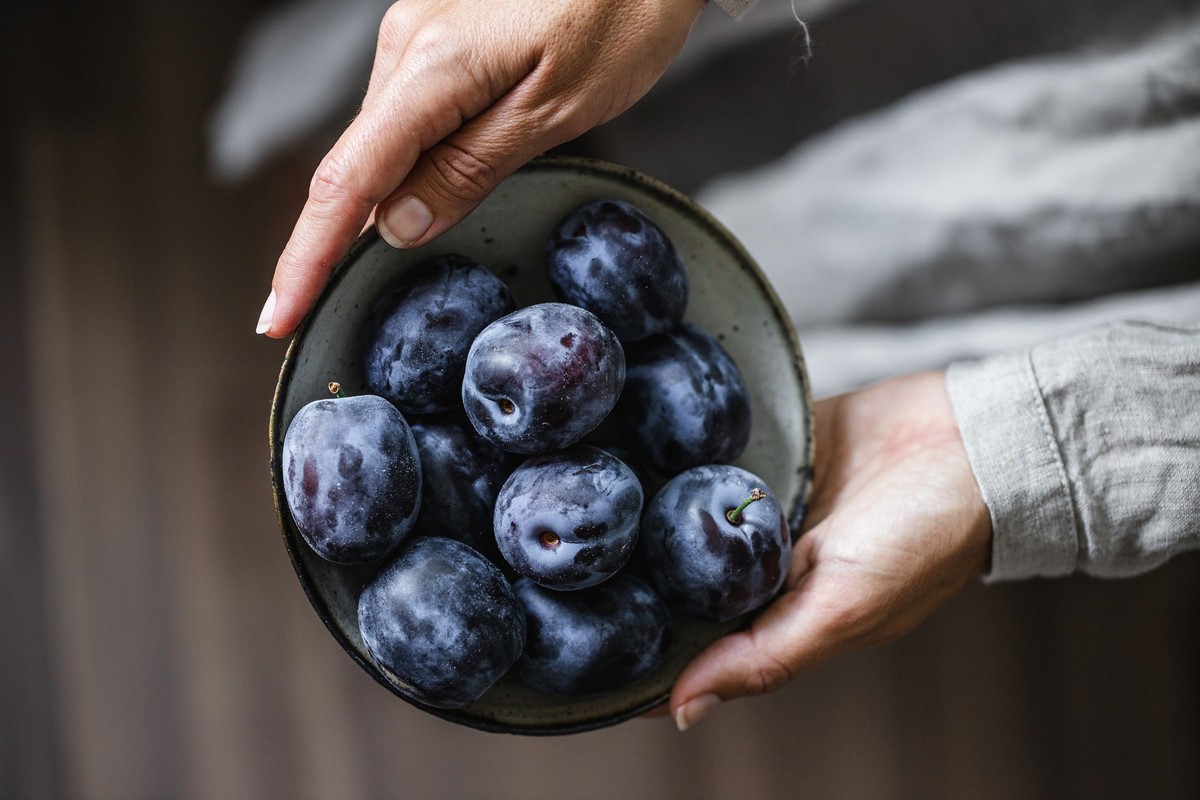 Close-up of woman hands holding blow of plums. Female with fresh plums in hands.