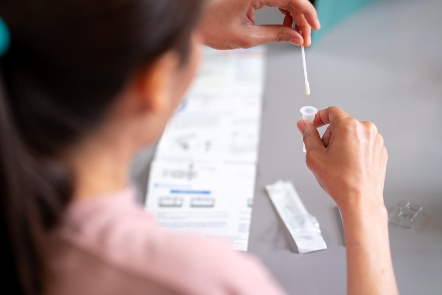 Asian woman using rapid antigen test kit for self test COVID-19 epidemic at home. Adult female place the fabric tip of the swab in the extraction tube and rolling around the tube. COVID-19 pandemic pr ...