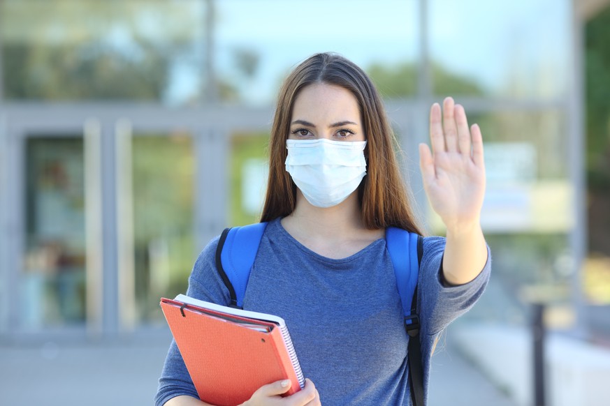 Front view of a student wearing a protective mask gesturing stop in a college campus