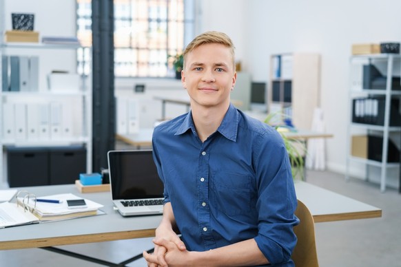 Friendly relaxed young businessman in the office turning in his chair to look at the camera with a warm smile