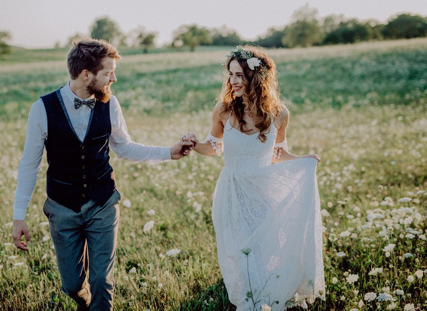 Beautiful young bride and groom outside in green nature at romantic sunset.