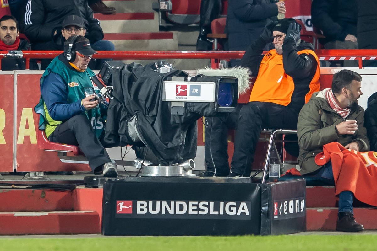ARCHIV - 30.11.2024, Berlin: Fußball: Bundesliga, 1. FC Union Berlin - Bayer Leverkusen, 12. Spieltag, An der Alten Försterei. Ein Kameramann hinter einer Kamera bei einem Fußballspiel mit Schriftzug: ...