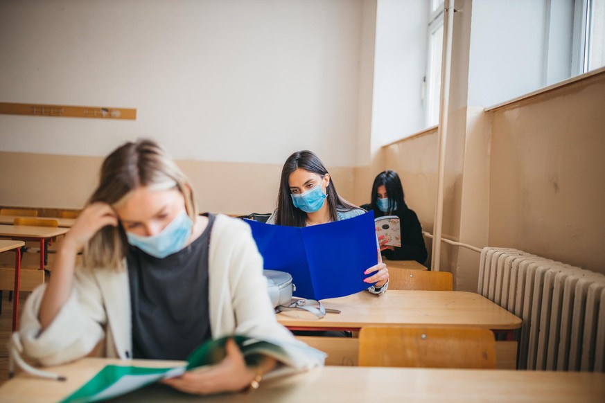 A view of high school students sitting at desks in a classroom with protective masks