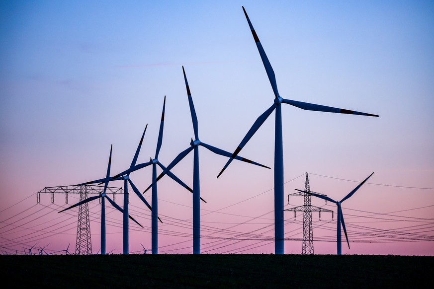 ARCHIV - 04.10.2022, Sachsen-Anhalt, Leuna: Windkraftanlagen und Hochspannungsleitungen sind vor dem Abendhimmel bei Leuna zu sehen. (zu dpa &quot;Linke will Gemeinden und Einwohner an Windkraft-Erlös ...