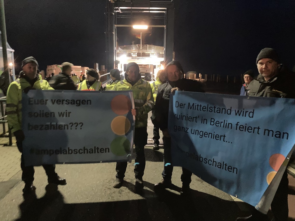 SCREENSHOT - 04.01.2024, Schleswig-Holstein, Sch�ttsiel: Landwirte stehen mit Plakaten mit der Aufschrift &quot;Euer Versagen sollen wir bezahlen??? #ampelabschalten&quot; am F�hranleger. W�tende Baue ...