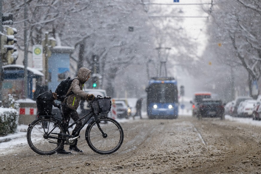 15.12.2022, Bayern, München: Eine Frau schiebt ihr Fahrrad über eine noch nicht vom Schnee geräumte Straße im Stadtteil Haidhausen. Nach dem Eisregen haben am Donnerstag Schneefälle in Bayern für Verk ...