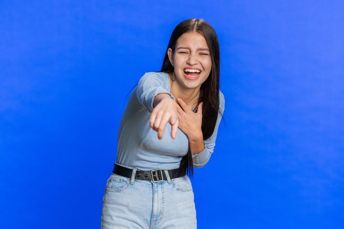 Amused lovely woman pointing finger to camera, laughing out loud, taunting making fun of ridiculous appearance, funny joke anecdote. Pretty brunette girl isolated alone on blue studio background xkwx  ...
