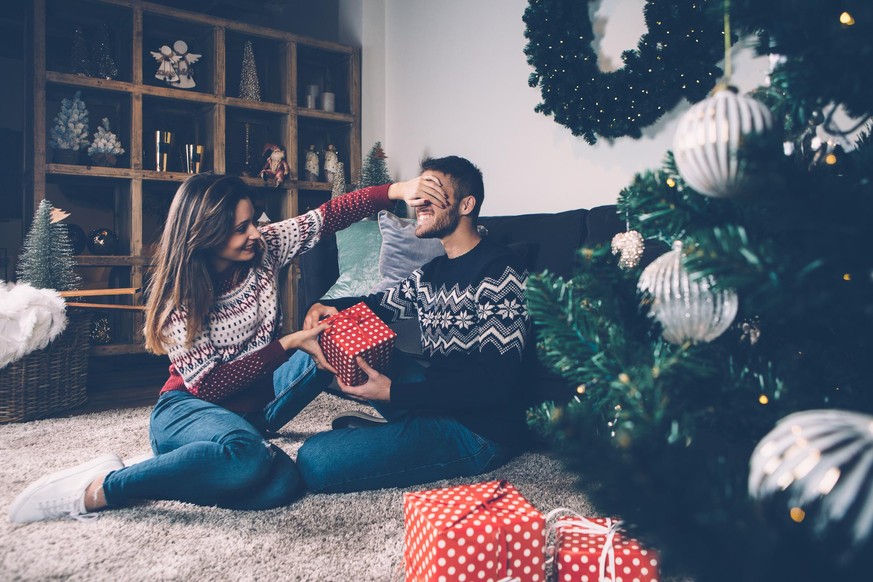 Young female laughing and closing eyes to boyfriend while giving him present.