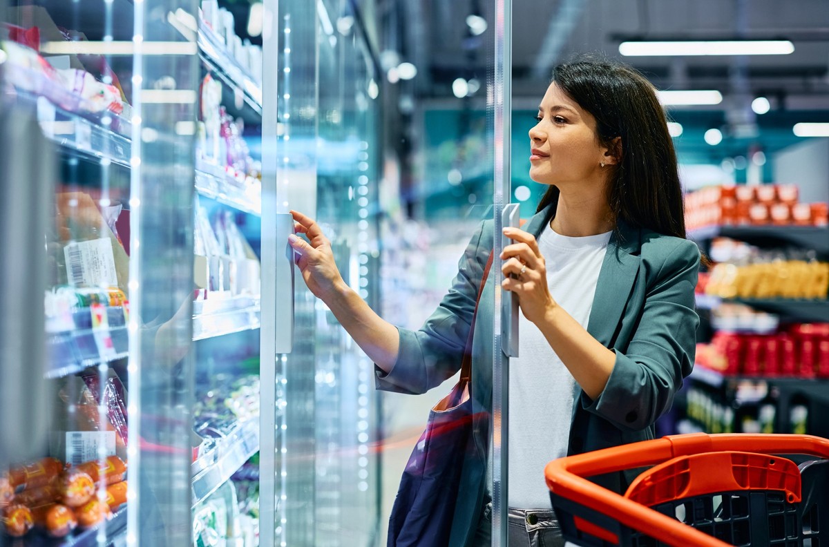 Smiling woman taking groceries from refrigerator while shopping in supermarket. Copy space.