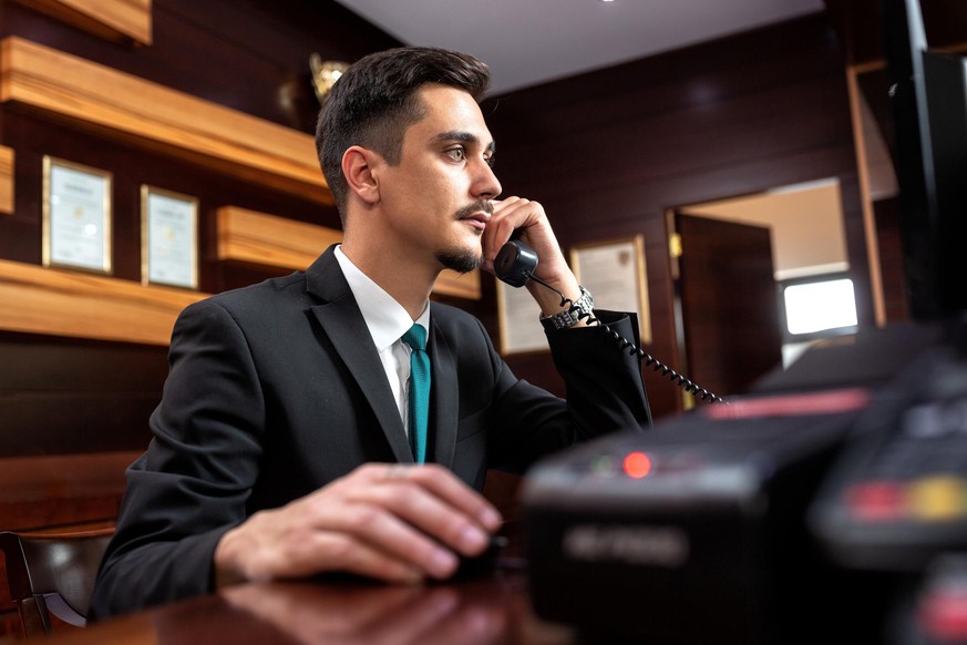 Smooth hotel reception worker talking on the phone, hotel operator