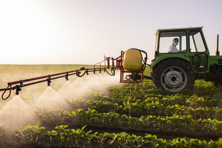 Tractor spraying pesticides on soy field with sprayer at spring