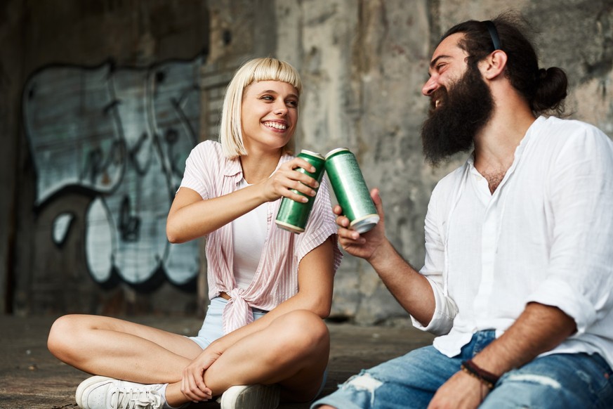 Young smiling couple toasting with beer cans in an urban environment