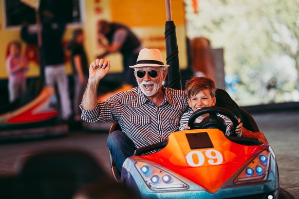 Grandfather and grandson having fun and spending good quality time together in amusement park. They enjoying and smiling while driving bumper car together.