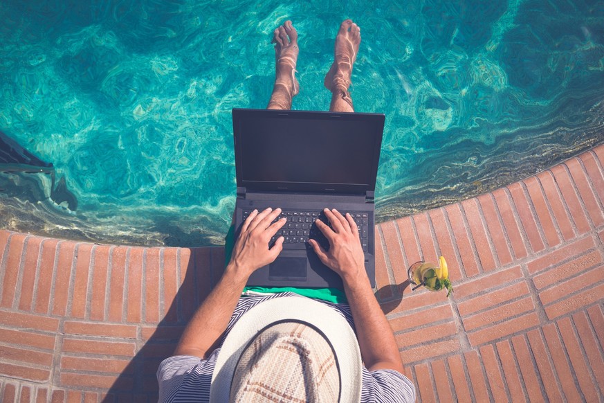High angle view of man sitting at the poolside and using laptop. Travel and technology concepts