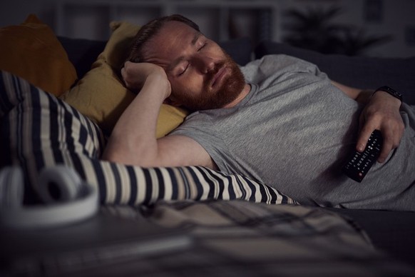 Portrait of bearded adult man sleeping on sofa while watching TV at night, copy space
