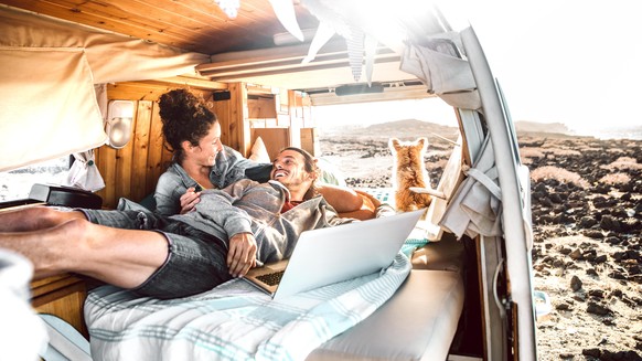 Hipster couple with dog traveling together on generic mini van transport - Digital nomad concept with indie people on minivan romantic trip working at laptop pc in relax moment - Warm contrast filter