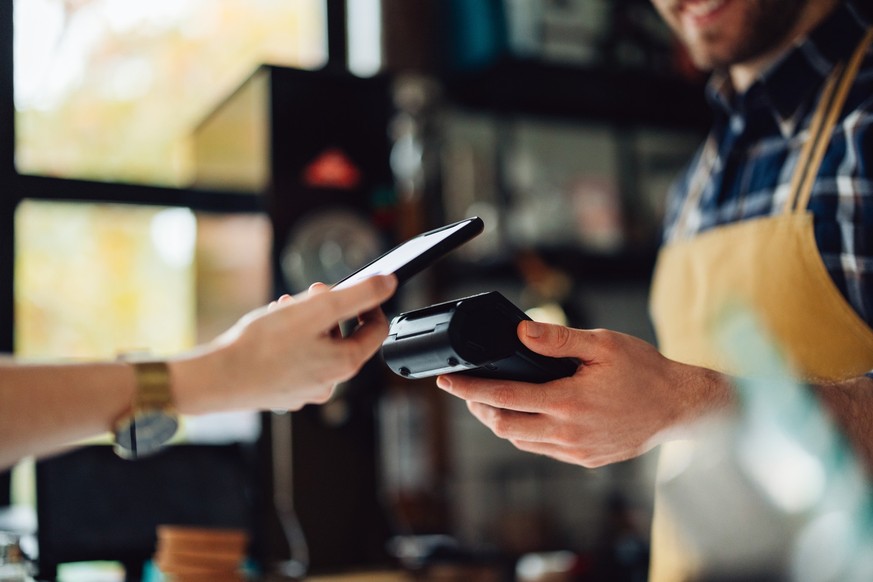 Unrecognizable people making an online payment. Anonymous man is holding a card machine while the other person is placing their phone to pay.