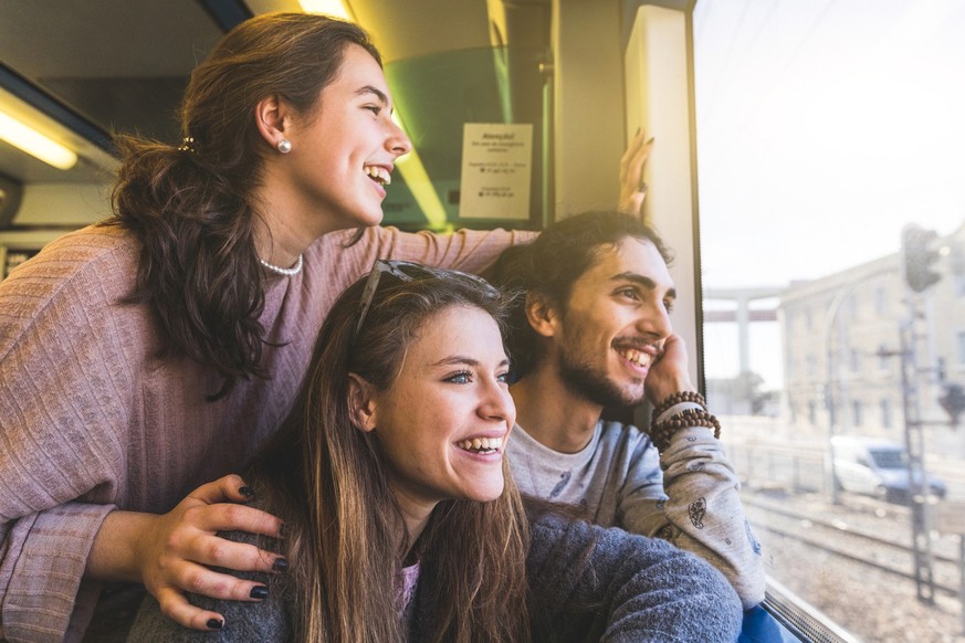 Happy group of friends looking out of train window while travelling on vacation together on a sunny day in Portugal - Smiling young man and women, copy space on the right