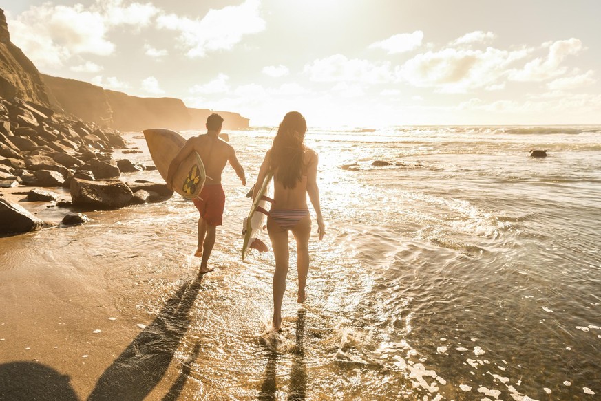 A man and women running into the ocean with their surf boards.