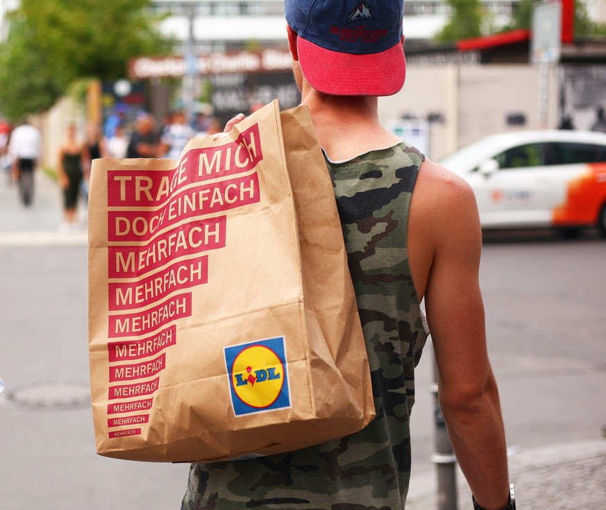 Ein junger Mann trägt am 17.08.2017 in Berlin im Bezirk Mitte an der Friedrichstraße eine Papiertüte von Lidl über der Schulter. Auf der Tüte steht &quot;Trage mich doch einfach mehrfach, mehrfach, me ...