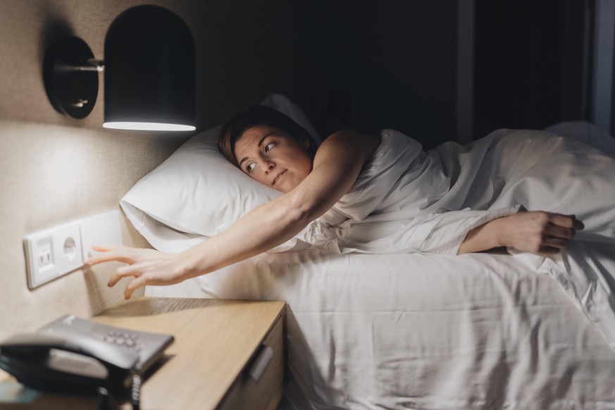 Mid adult woman turning off light while lying on bed model released Symbolfoto property released DGOF02090