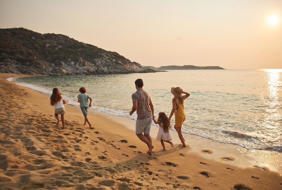 A family run hand in hand down a tropical paradise beach during sunset.